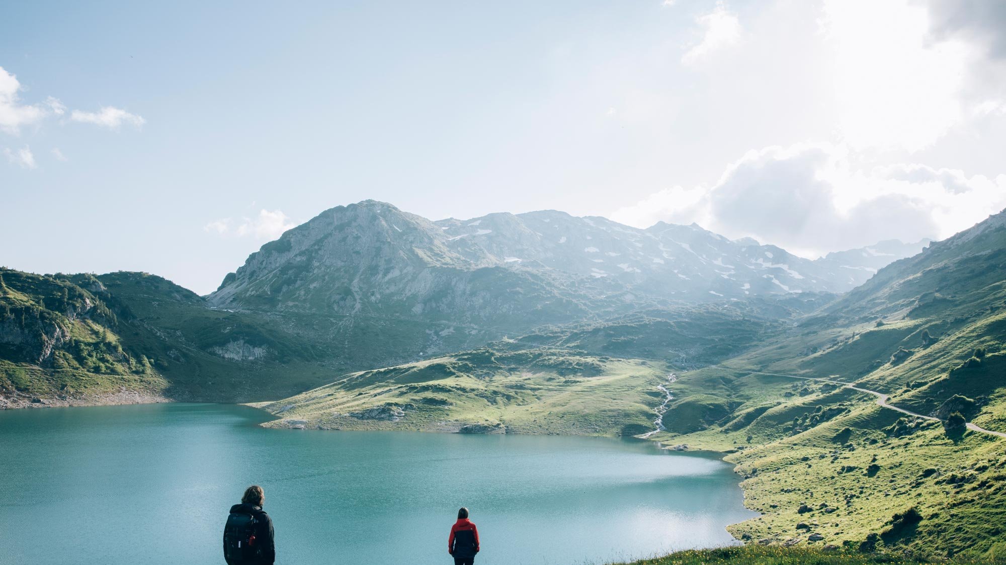 Zwei Wanderer gehen am ruhigen Lechsee, umgeben von Bergen und grünem Wald im Freien.