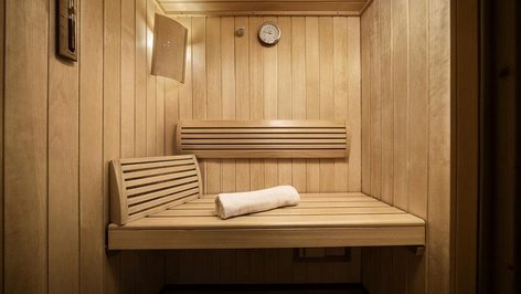 Innenansicht einer Holzsauna mit einer Bank, einem Handtuch und einer Wanduhr sichtbar.