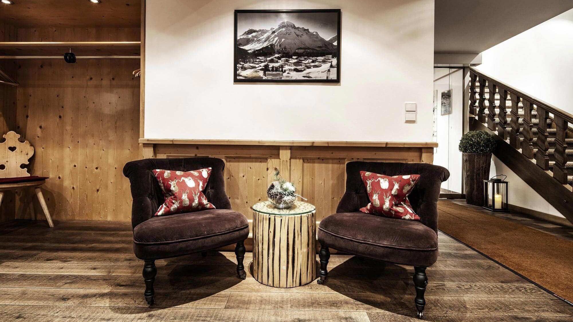 Sitzbereich mit zwei gepolsterten Stühlen, einem Holztisch und Bergfotografie an der Wand