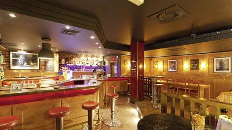 Interior view of a cozy bar featuring wooden counter and high stools with ambient lighting