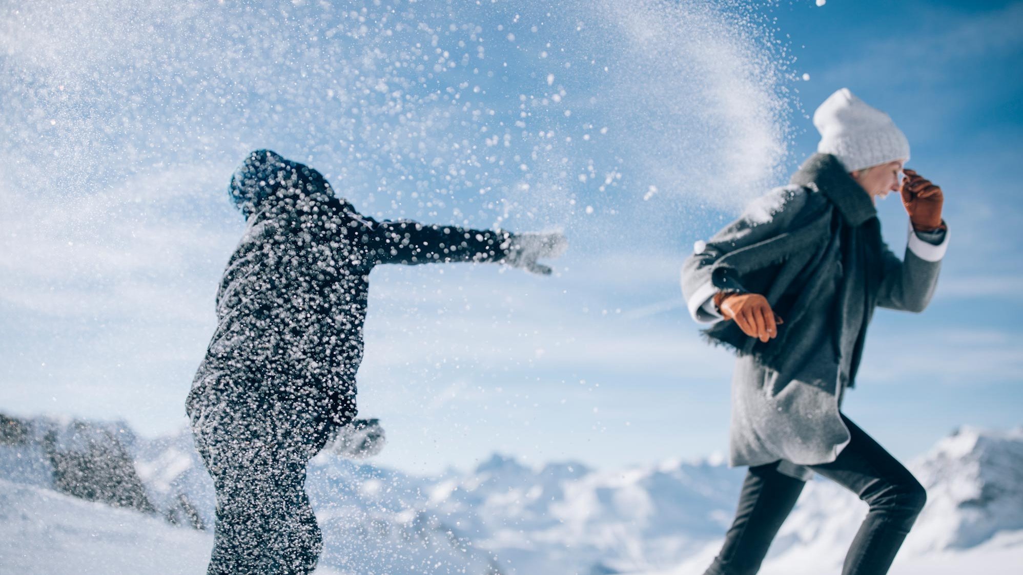 Zwei Personen werfen sich Schneebälle in einer verschneiten Berglandschaft zu. Schöne Winteraktivität im Freien.