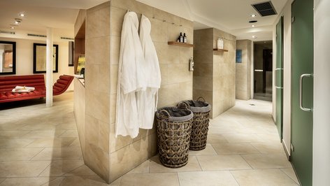 Spacious relaxation area in a modern spa featuring red seating and bathrobes on the wall