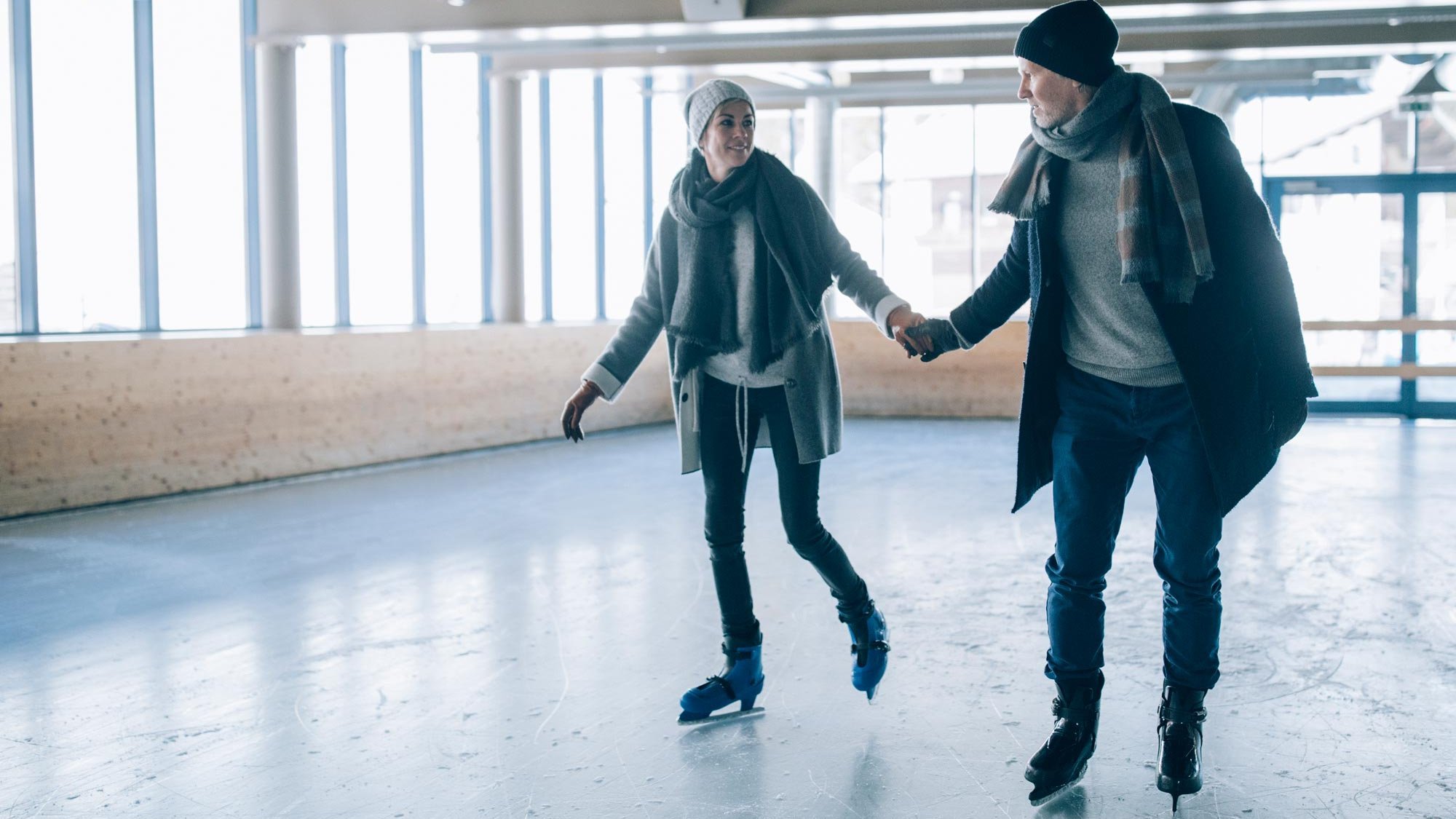 Paar beim Eislaufen in einer Halle, Hand in Hand auf dem Eis aktiv unterwegs, fröhlich.