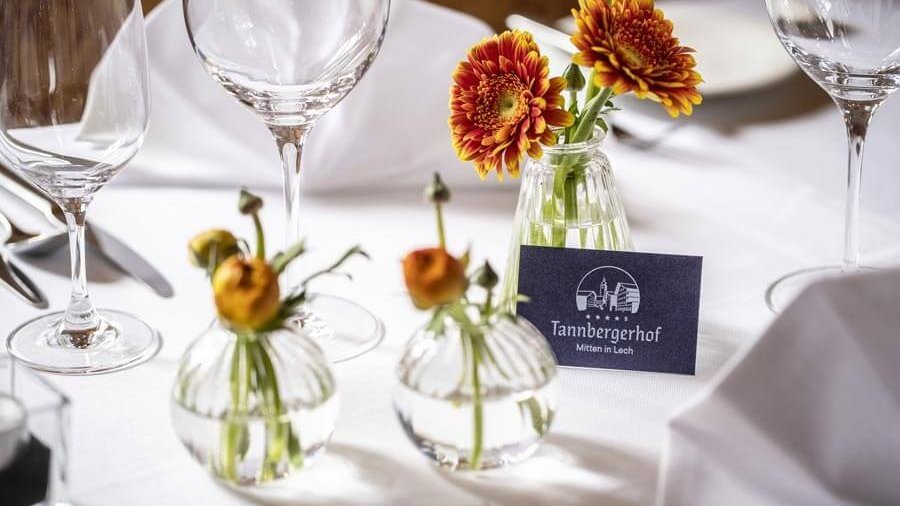 Ein stilvoll gedeckter Tisch mit Gläsern, Besteck und floralen Arrangements in Vasen.