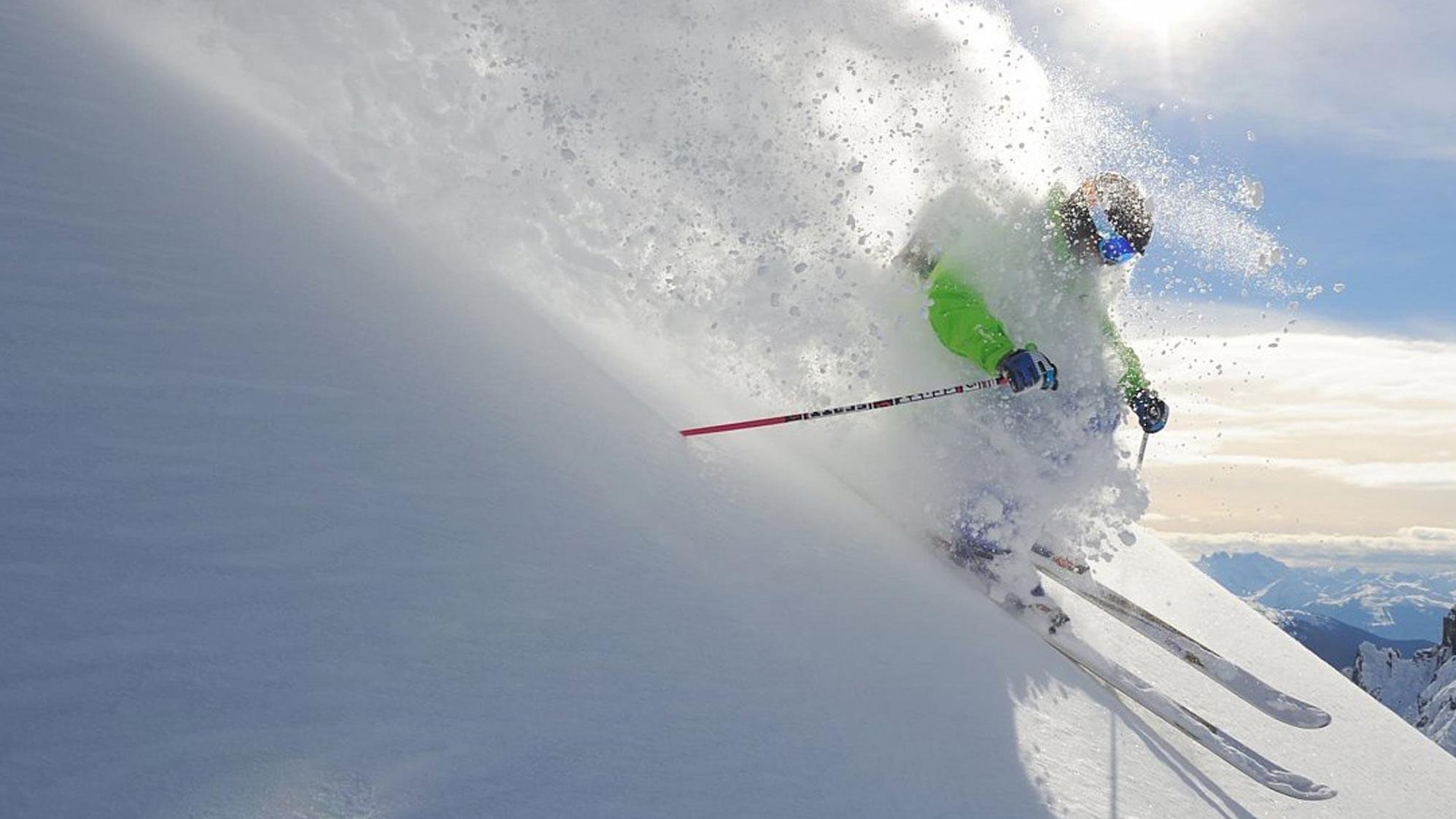 Skifahrer fährt durch unberührten Schnee auf einer Berghanglinie bei Sonnenschein