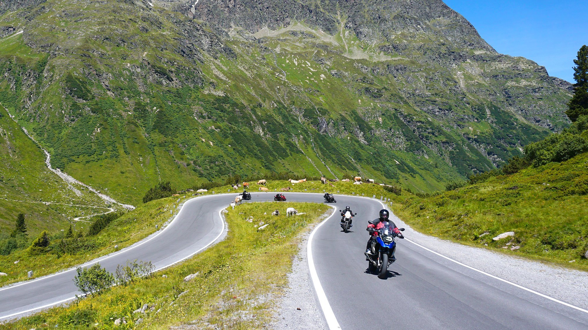 Motorcycles riding on a winding mountain road surrounded by hills and rocky peaks