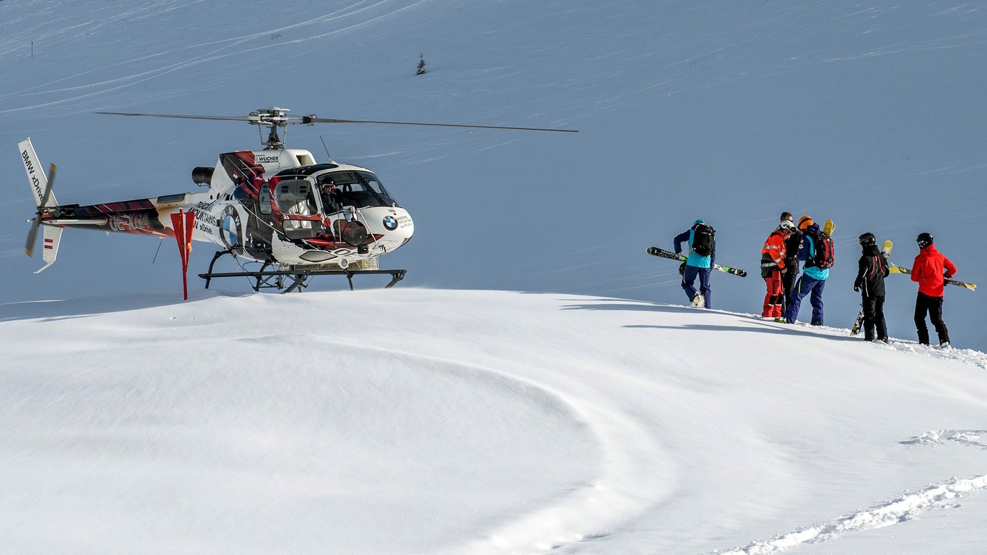 Gruppe von Skifahrern und Snowboardern nähert sich einem Hubschrauber in schneebedeckter Berglandschaft