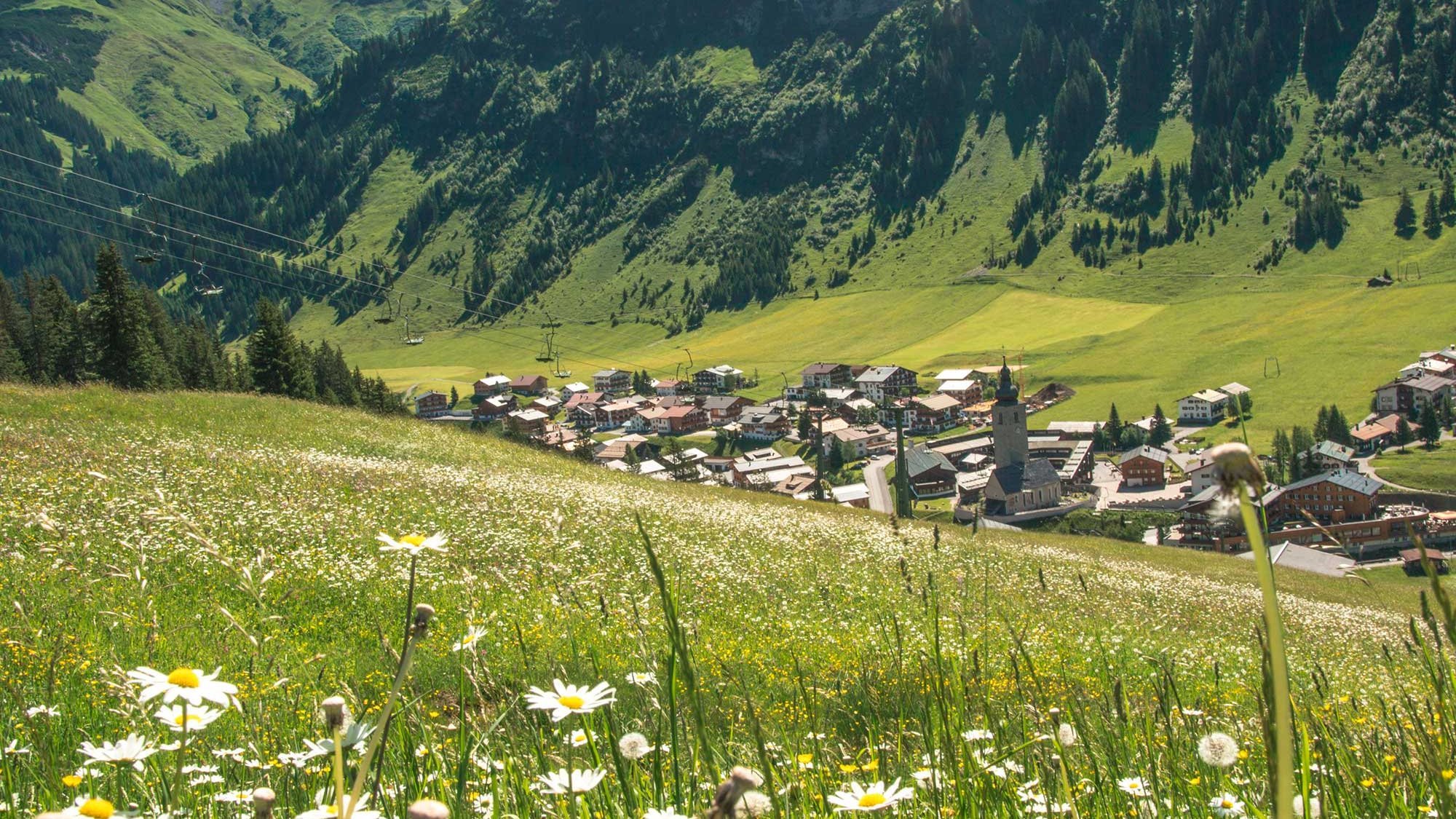 Bergdorf umgeben von Bergen und blühenden Wildblumen in einem Tal der Alpenregion