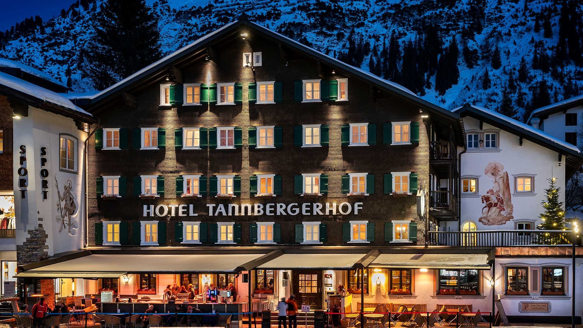Mehrstöckiges Hotel mit beleuchteten Fenstern vor schneebedeckten Bergen bei Nacht