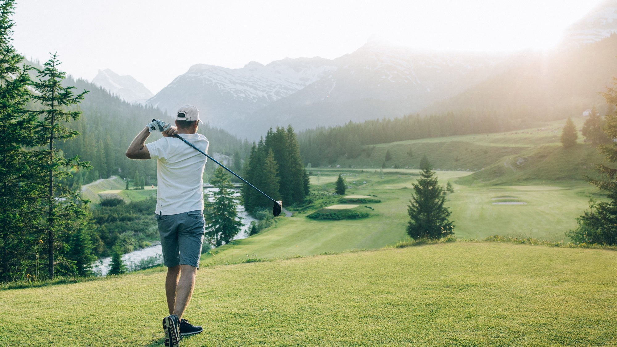 Ein Golfer führt einen Schwung auf einem Golfplatz mit Bergen im Hintergrund aus.