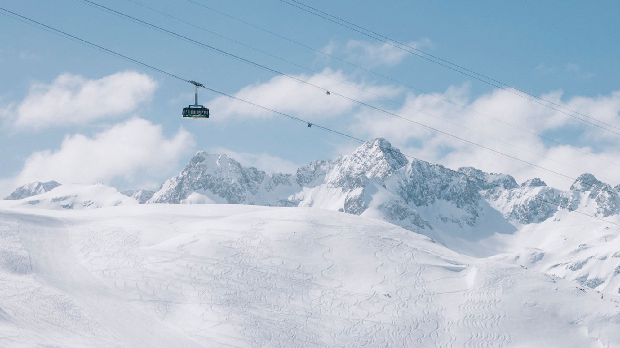 Seilbahn fährt über verschneite Berglandschaft mit klar blauem Himmel im Hintergrund