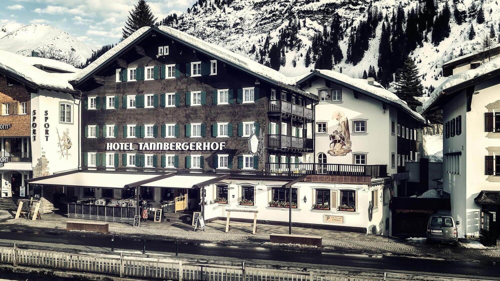 Außenansicht des Hotels Tannbergerhof mit schneebedeckten Bergen im Hintergrund.