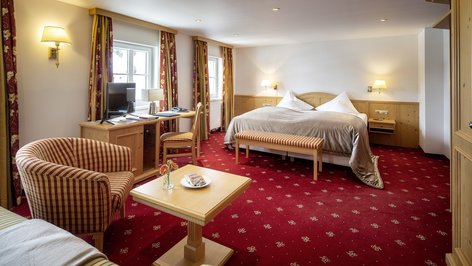Spacious hotel room featuring a large bed, seating area with striped chair, and desk with computer