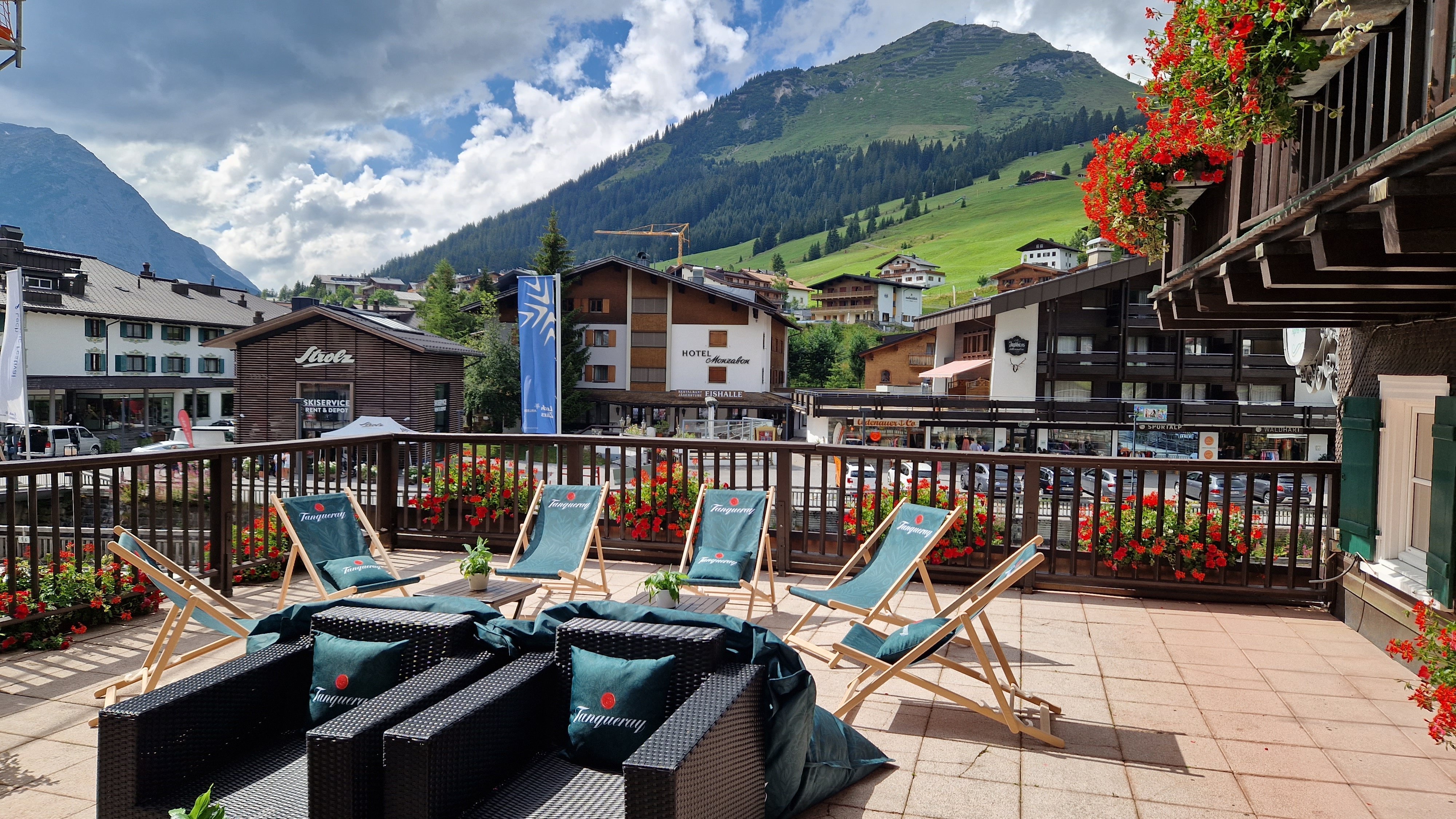 Terrasse mit Sitzgelegenheiten und Blick auf ein alpines Dorf umgeben von Bergen