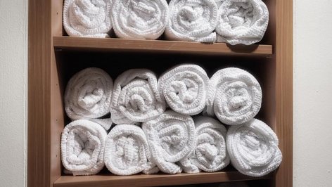 Stack of white towels organized on a wooden shelf in a bathroom setting for easy access
