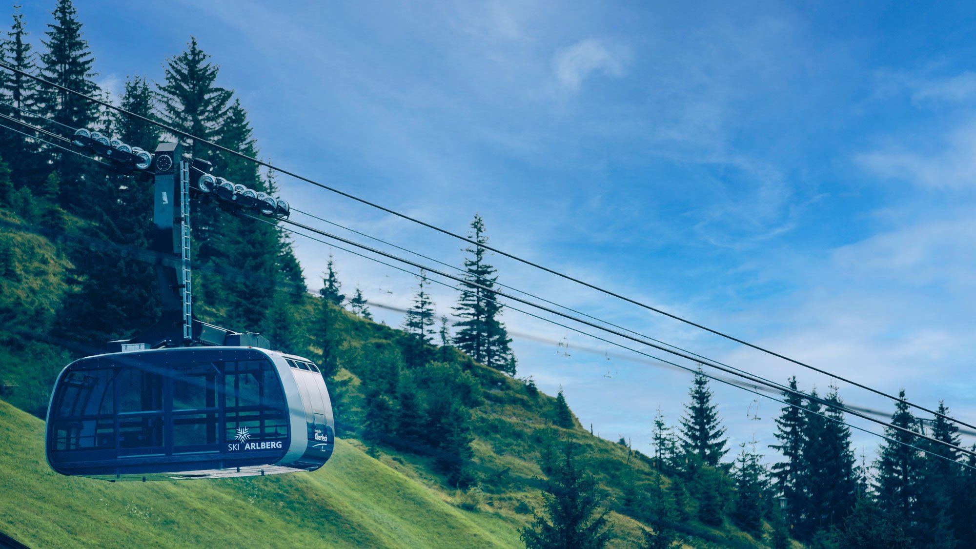 Seilbahn fährt über grüne Berge unter blauem Himmel in den Alpen bei Lech Zürs am Arlberg.