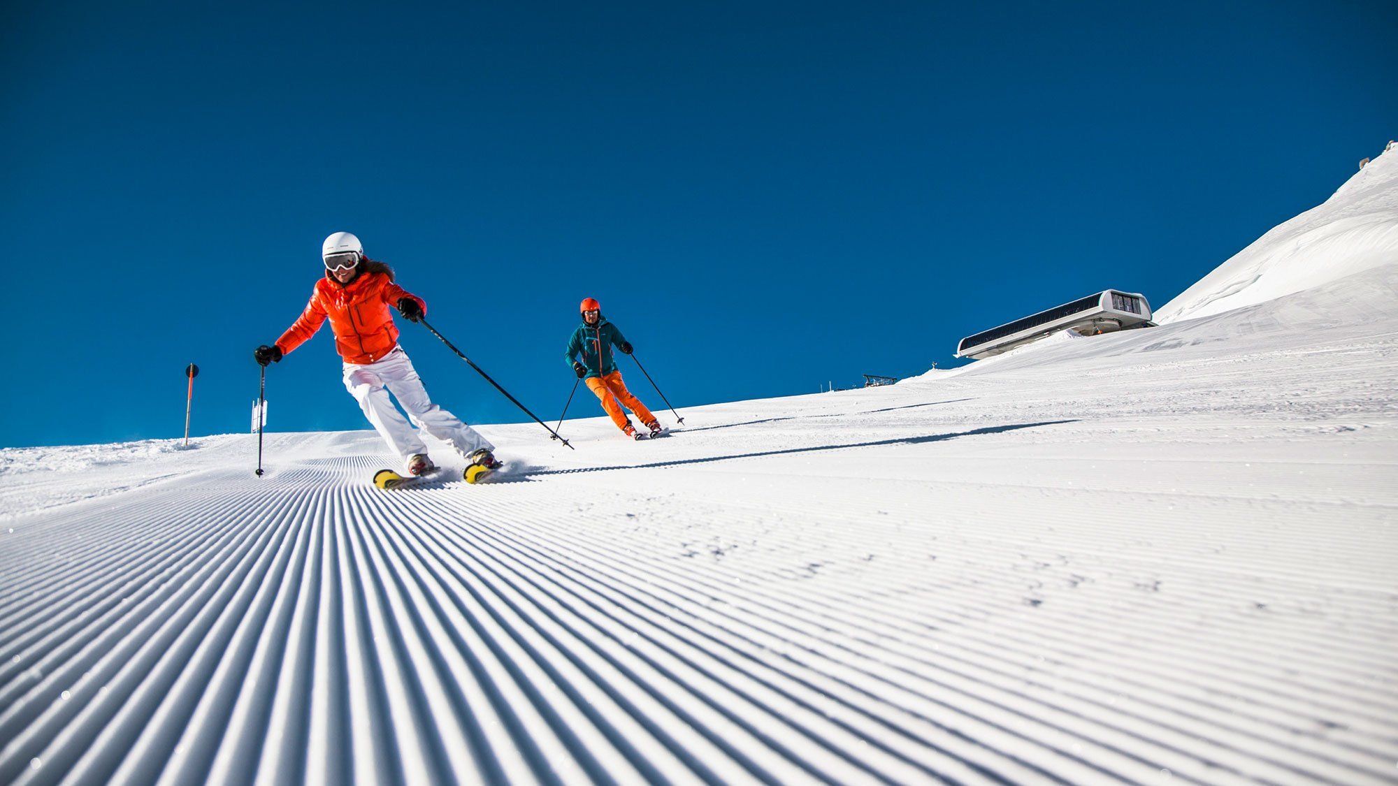 Zwei Skifahrer auf einer frisch präparierten Piste unter blauem Himmel in den Bergen