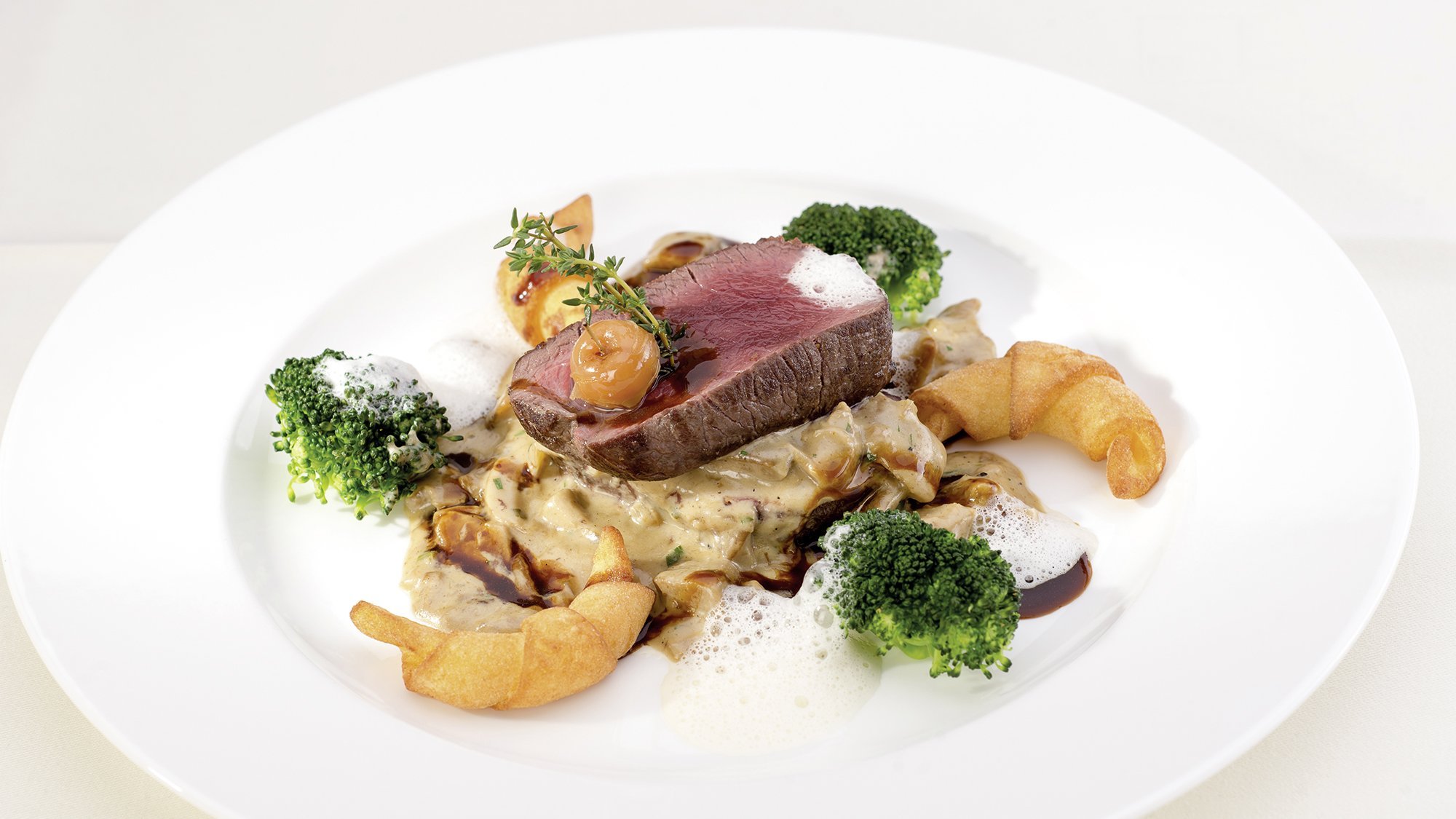 Ein Beef Steak mit Brokkoli und cremiger Sauce elegant angerichtet auf einem Teller.