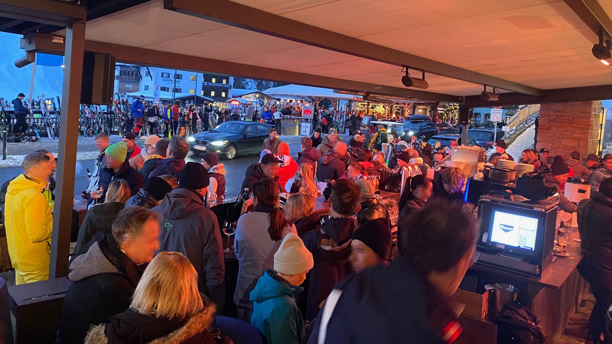 Menschen versammeln sich an einer belebten Außenbar in einem Skigebiet bei Abenddämmerung