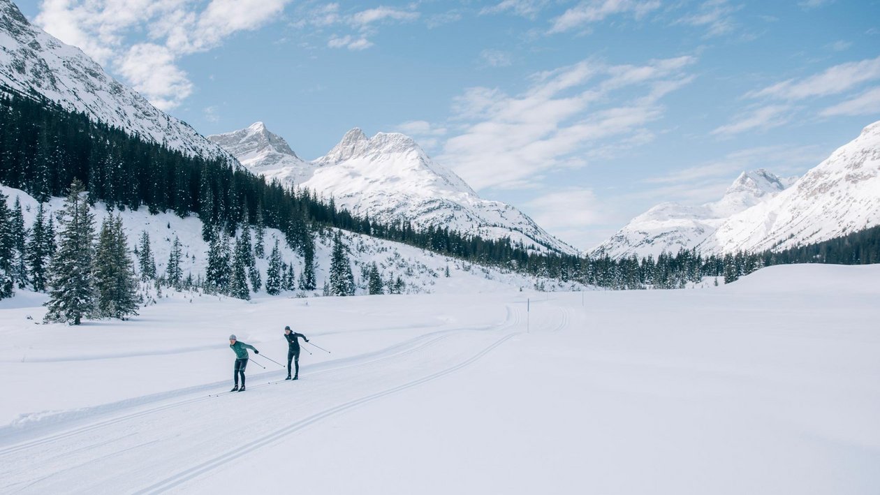 Winter Adventure in Arlberg Two cross-country skiers navigating a snowy landscape with mountains and pine trees