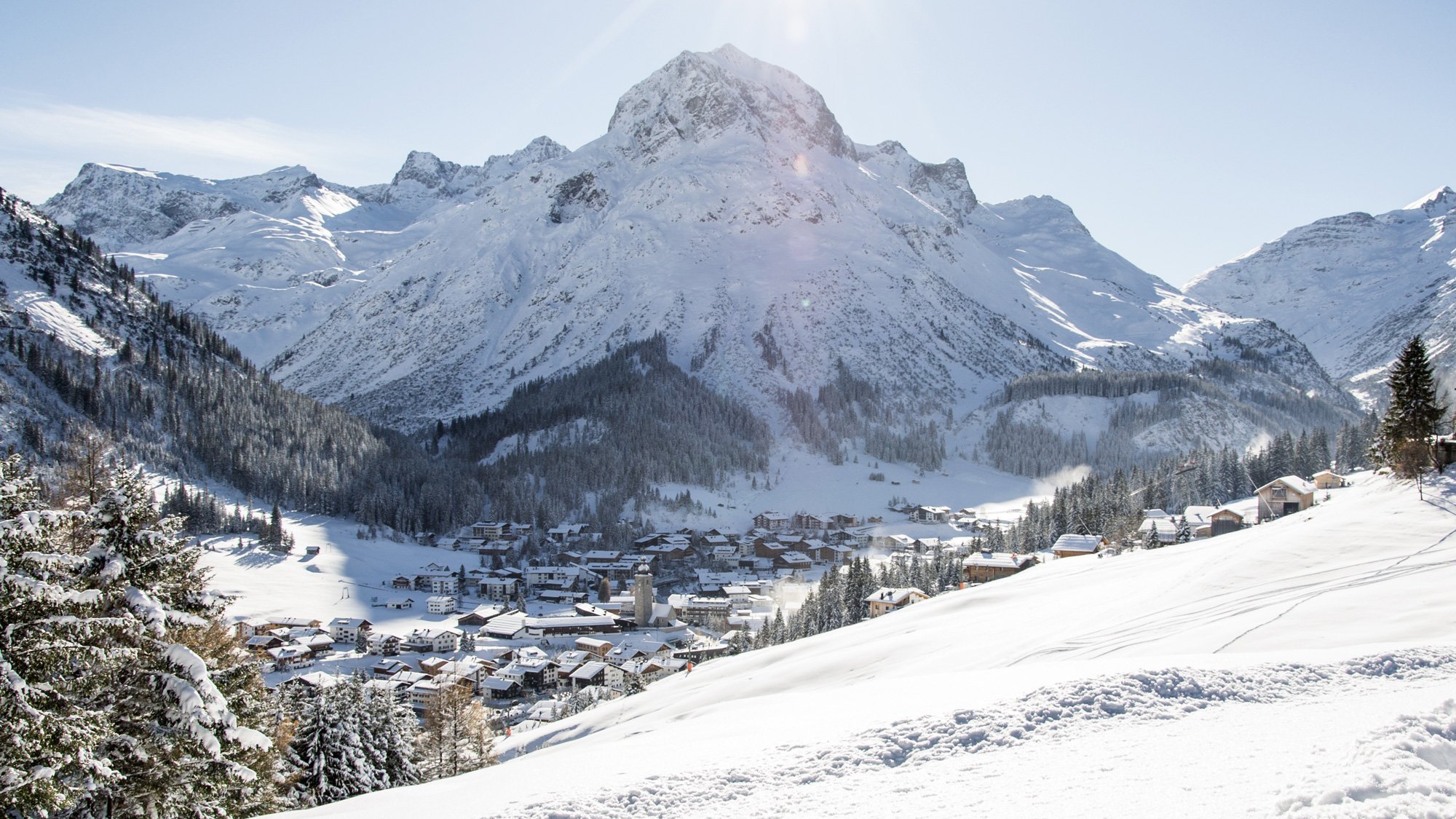 Winterlandschaft mit schneebedeckten Bergen und einem kleinen Bergdorf im Tal sichtbar.