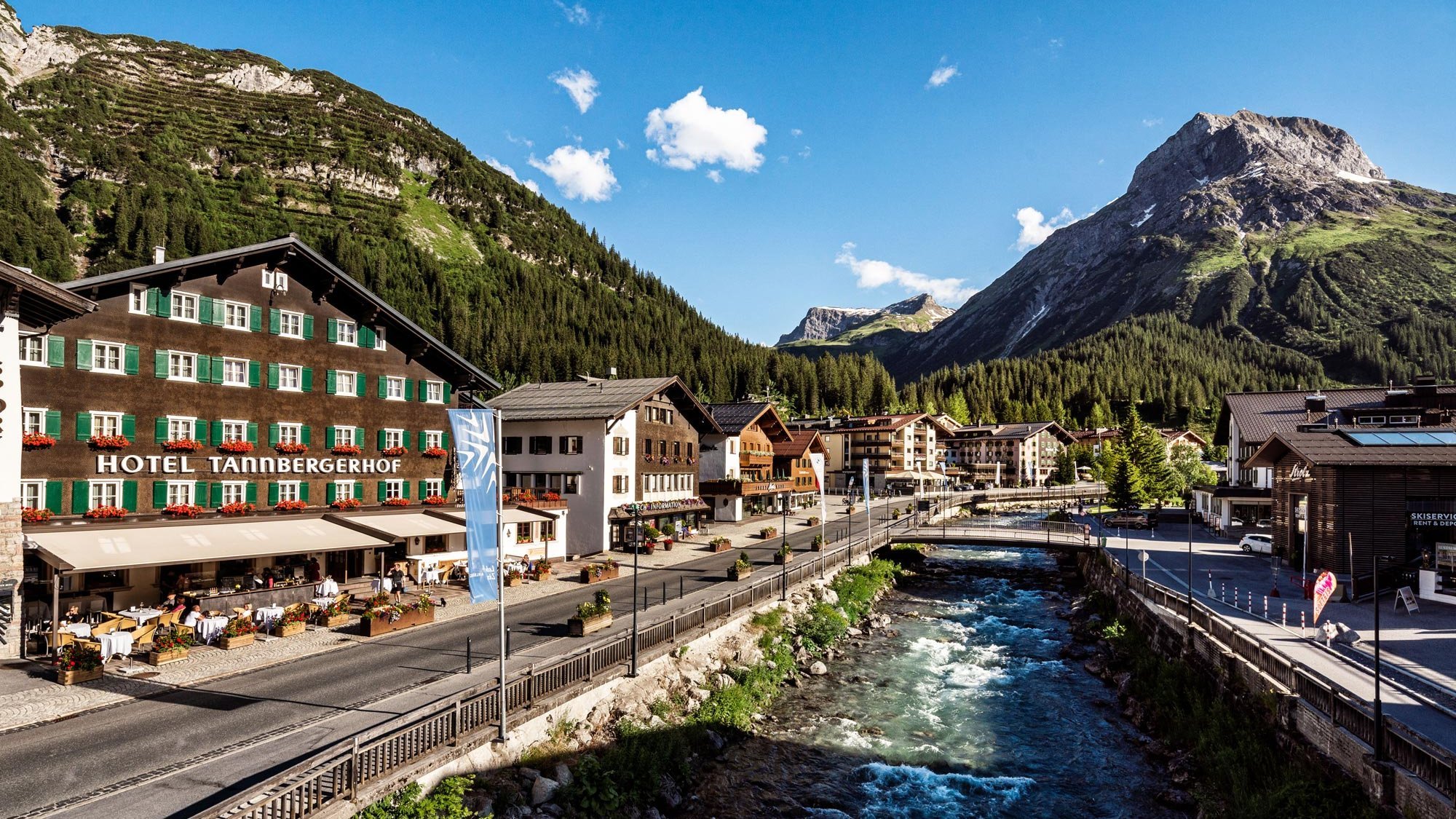 Pittoreskes Alpen-Dorf mit einem Hotel, umgeben von Bergen und einem fließenden Fluss