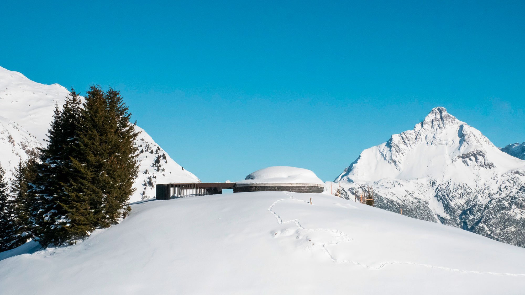 Alpine Landschaft mit schneebedecktem Hang und moderner Architektur unter klarem Himmel