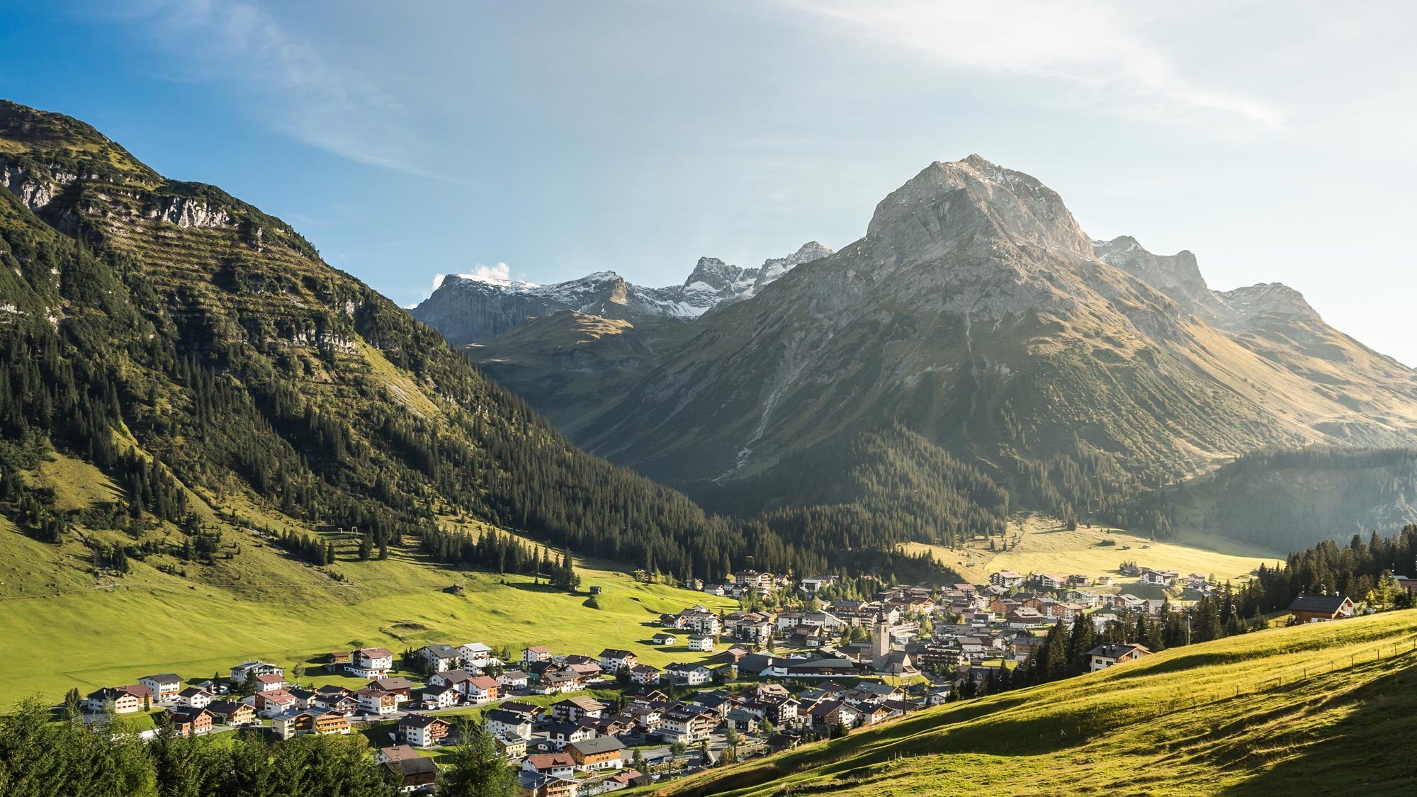 Blick auf ein malerisches Bergdorf umgeben von hohen Bergen und üppigem Grün im Tal.