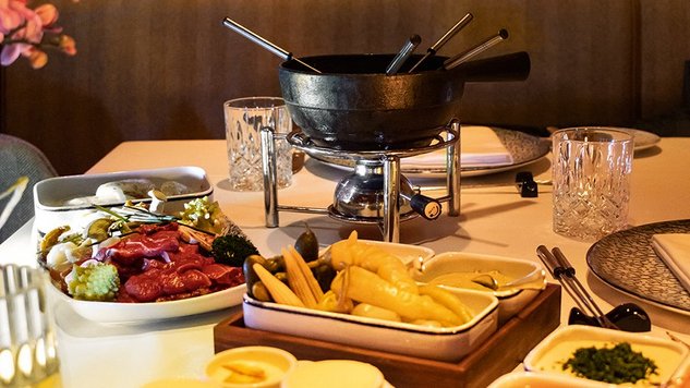 Savor the Experience of Hot Pot Dining Fondue set with meat, vegetables, sauces and side dishes on a laid table at the Tannbergerhof in Lech © Robert Stocker