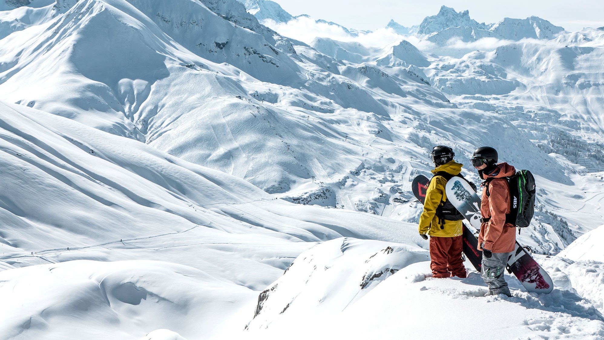 Zwei Snowboarder stehen auf einem schneebedeckten Berggipfel mit weitem Blick über die winterliche Landschaft