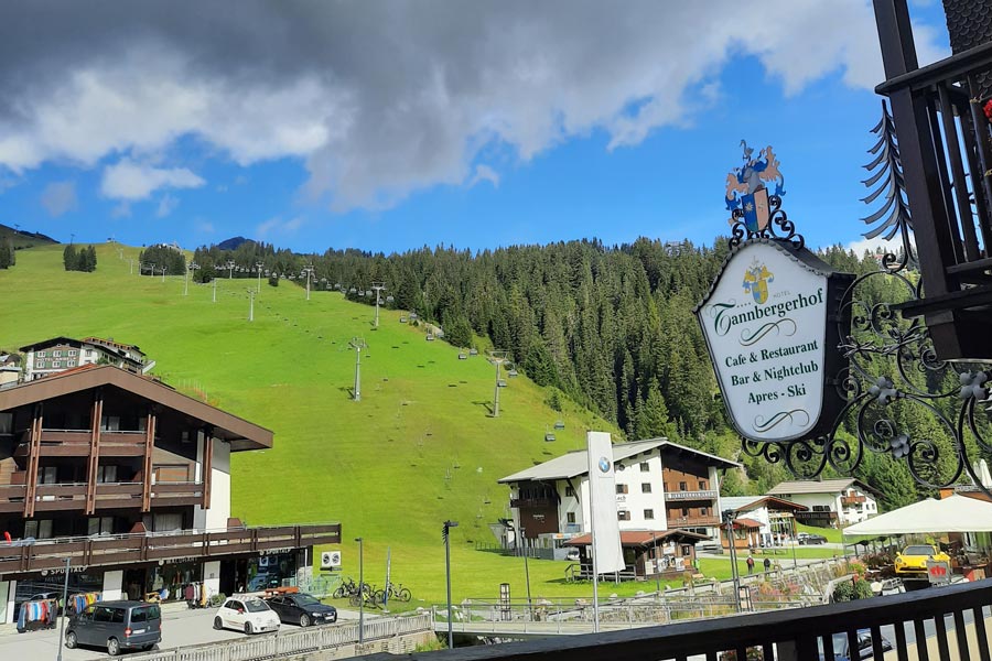 Aussicht auf eine grünen Abhang mit Wander- & Skiliften. Davor ist das Schild des Hotels Tannbergerhof zu sehen