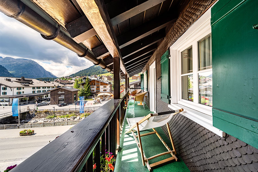 Balkon mit Holzgeländer, zwei Liegestühlen und Blick auf Lech und die umliegende Berglandschaft am Arlberg © Foto Lehmann