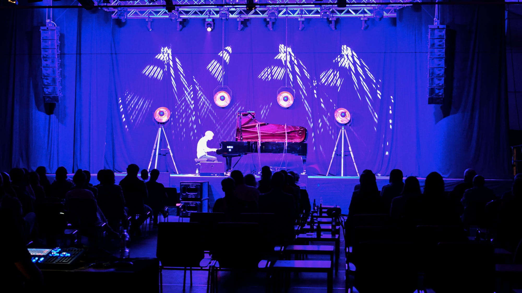 Pianist spielt live auf einer Bühne vor Publikum mit dramatischer Beleuchtung und visuellen Effekten.